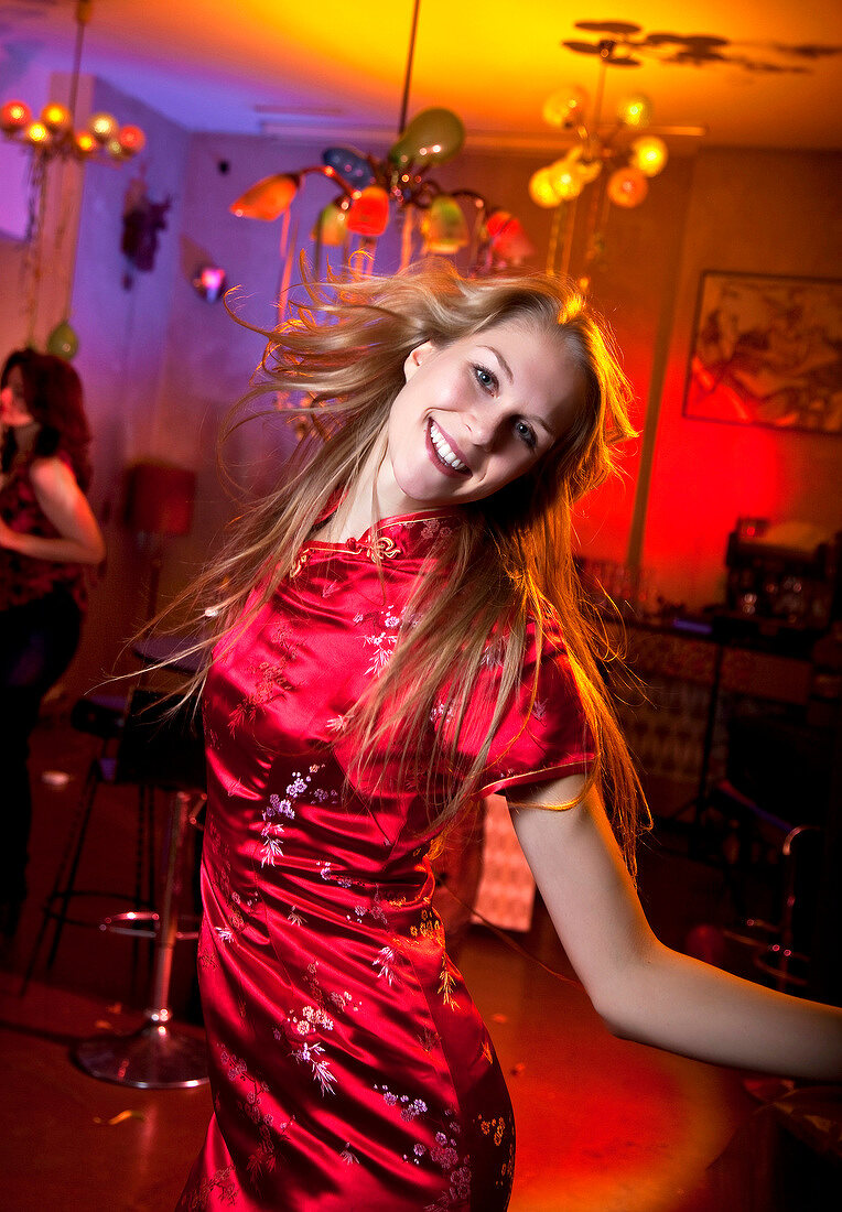 Happy woman wearing red satin dress celebrating while dancing at New Year's Eve party