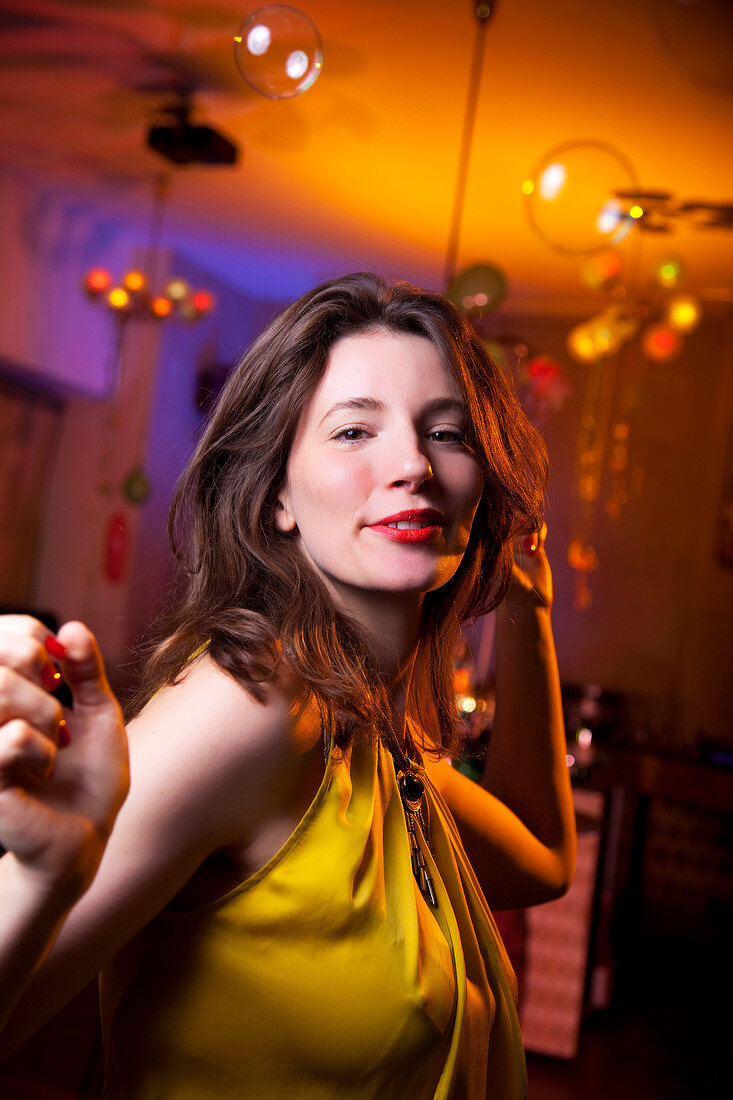 Portrait of happy woman in yellow top dancing while celebrating New Year's, smiling