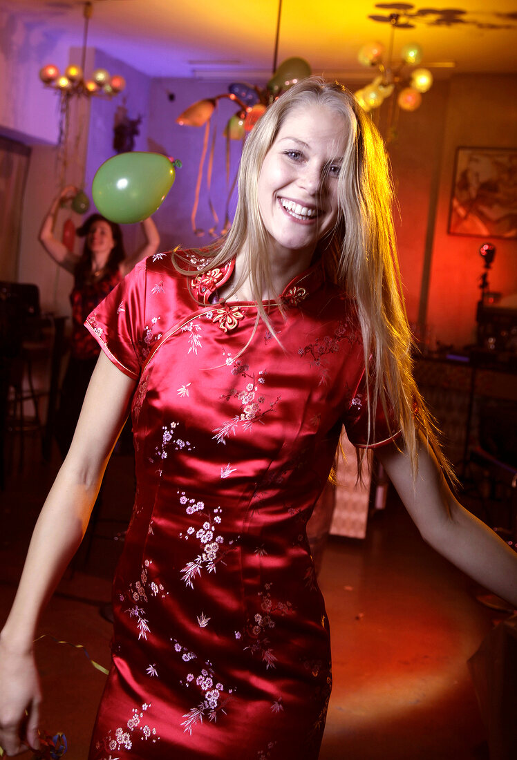 Frau im roten Satinkleid feiert und tanzt auf einer Silvesterparty