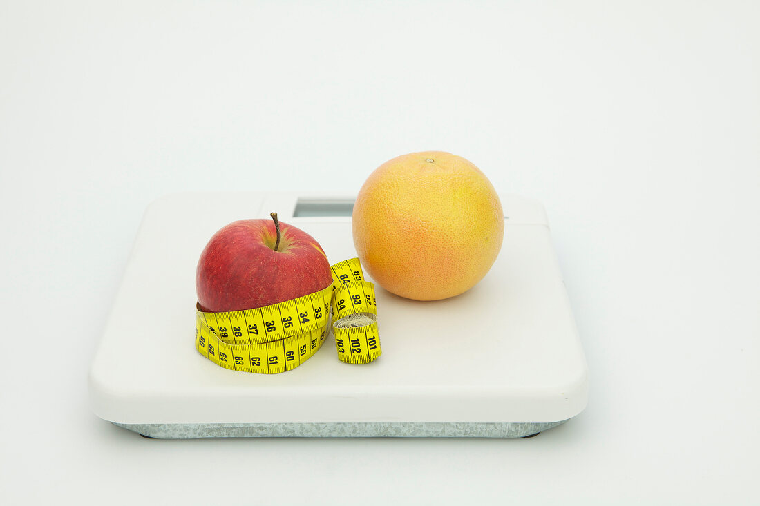 Symbolbild für Diät, Apfel mit Maßband und Grapefruit auf Waage