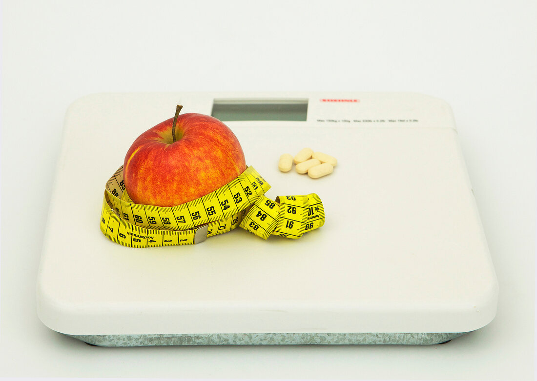Apple with measuring tape and pills on weighing scale, Icon image for diet