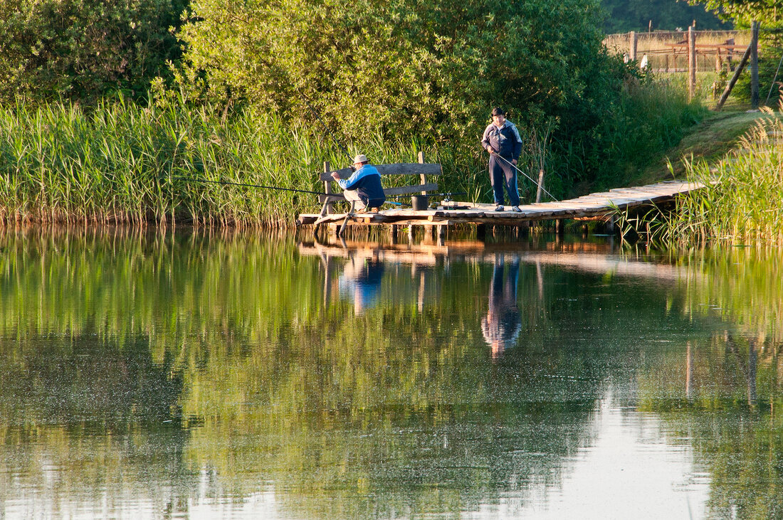 Two men fishing on jetty of Masurian Lake District, Mikolajki, Warmia Masuria, Poland