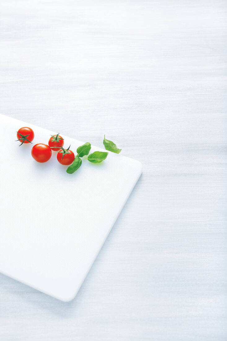 Tomatoes and basil leaves on chopping board
