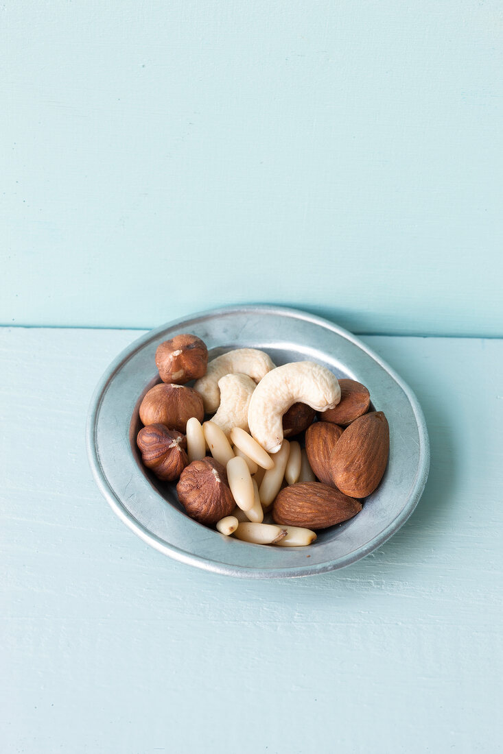 Plate of different nuts on blue background