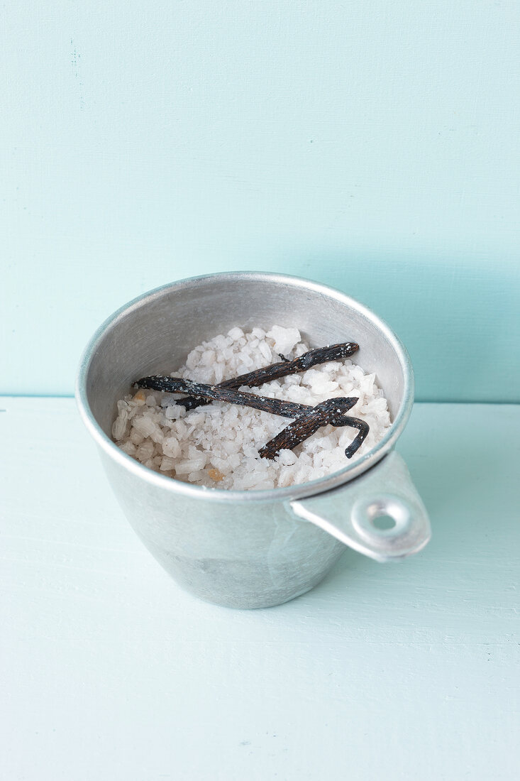 Bowl of salt and vanilla on blue background