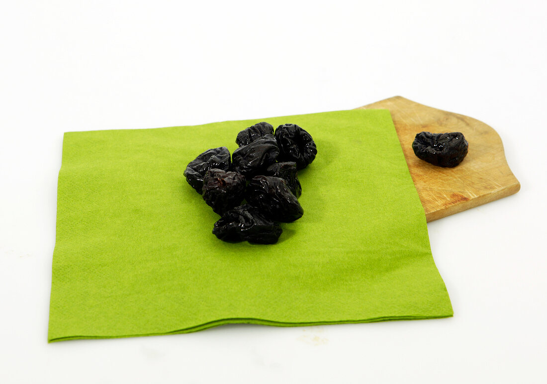 Dry plums on green cloth with wooden platter on white background