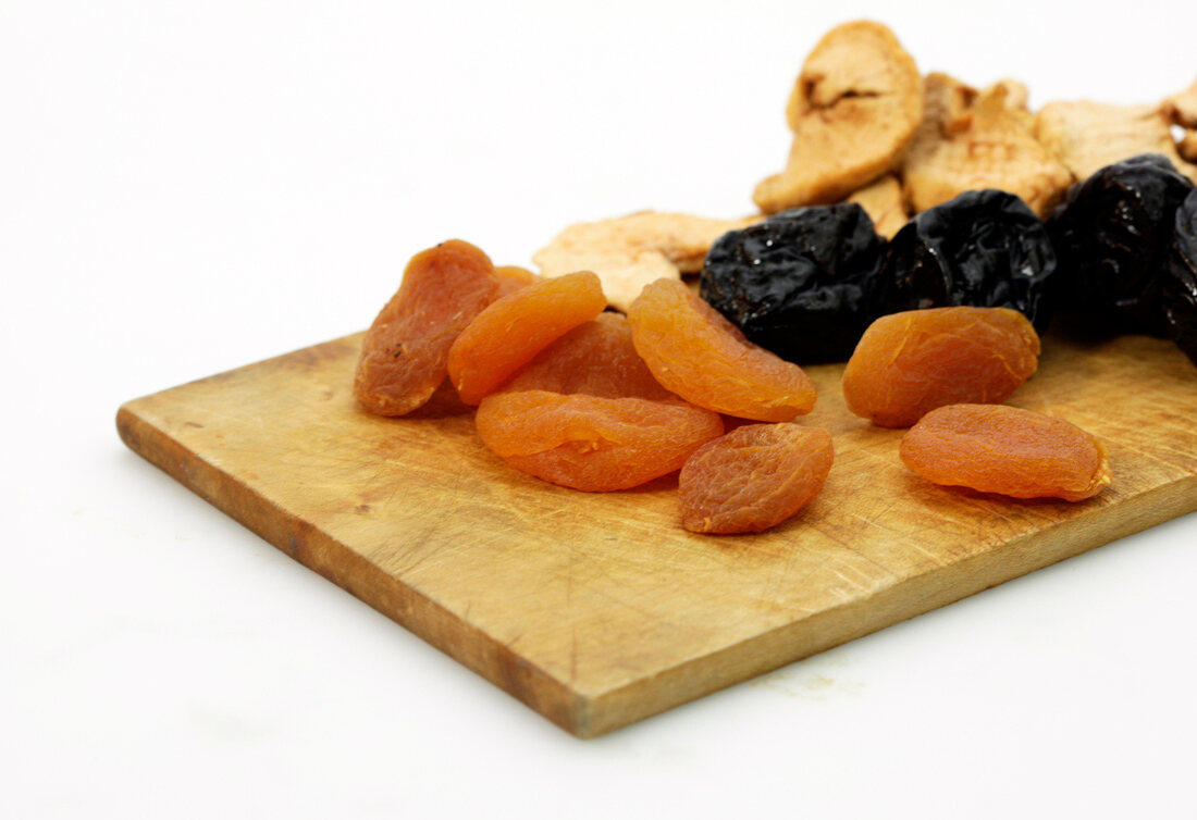 Mixed dry fruits on wooden platter on white background