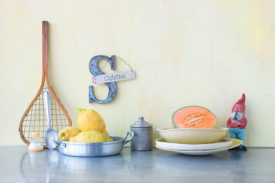 An arrangement featuring crockery, a garden gnome, fruit and a decorative letter S