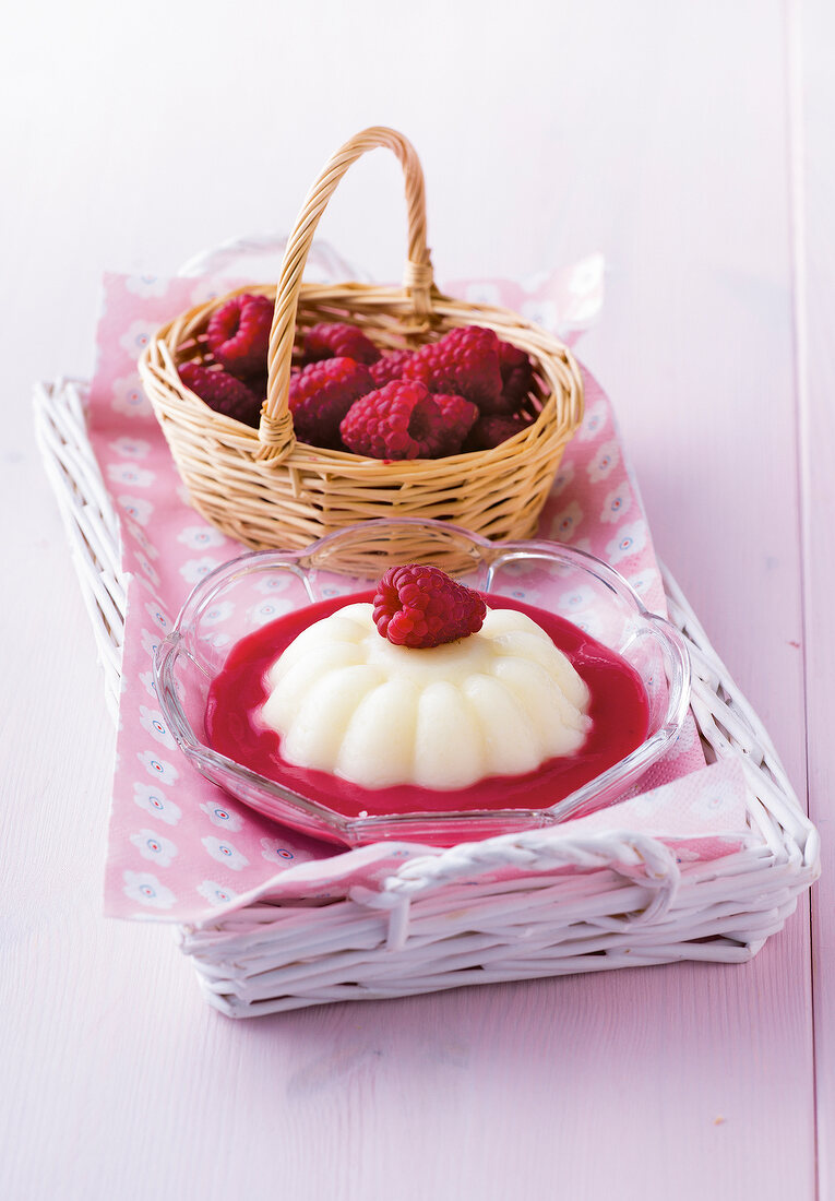 Custard with raspberry sauce in glass bowl and basket of raspberries