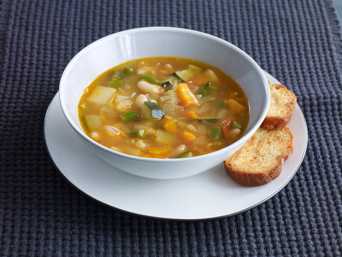 Minestrone soup in bowl with garlic crostini on plate