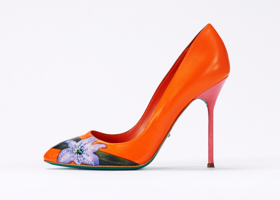 Close-up of orange stiletto pumps with flower patch on white background