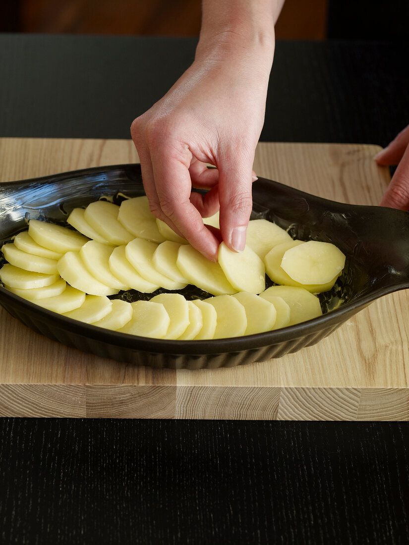 Close-up of hand arranging sliced potatoes in baking tray, step 2