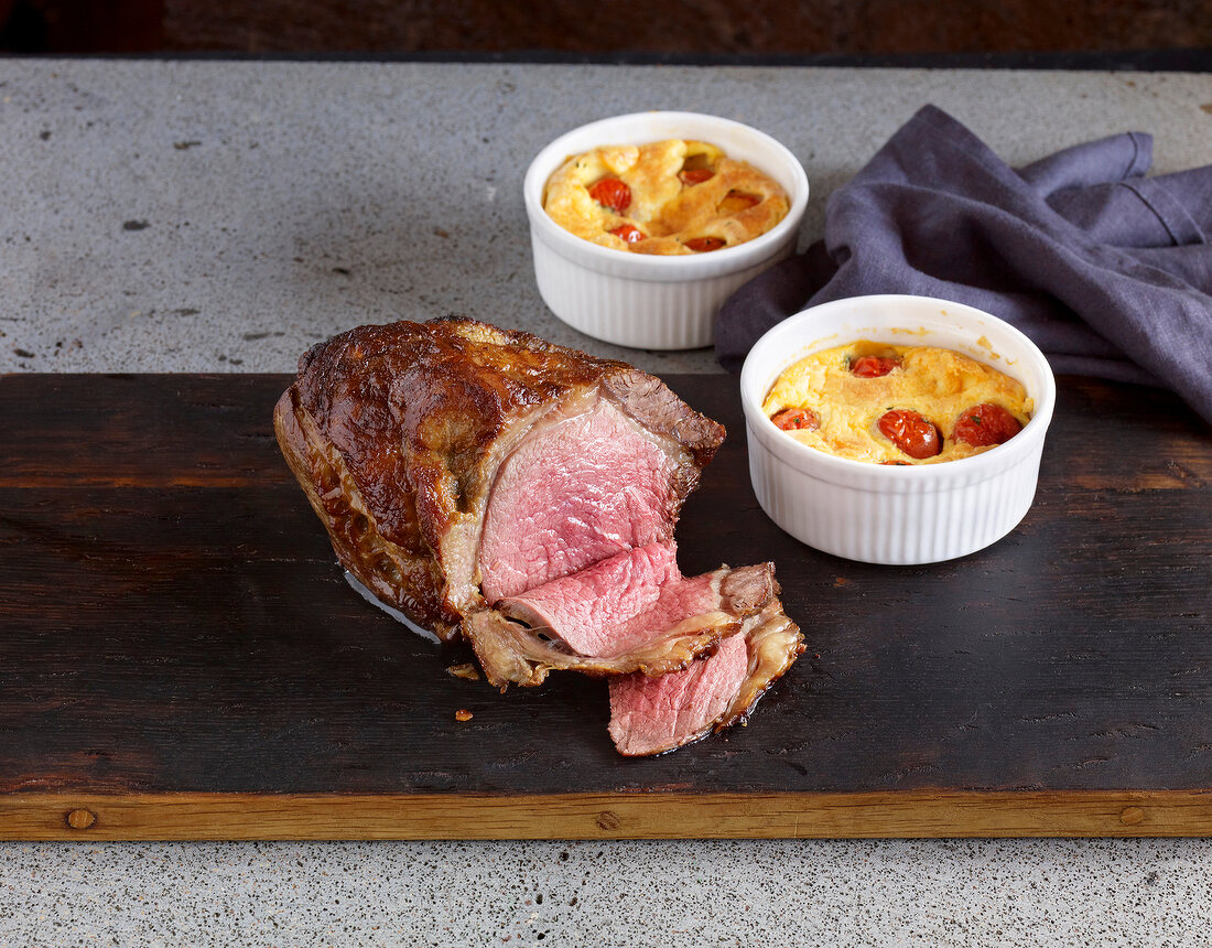 Roasted beef with tomato clafoutis on wooden board