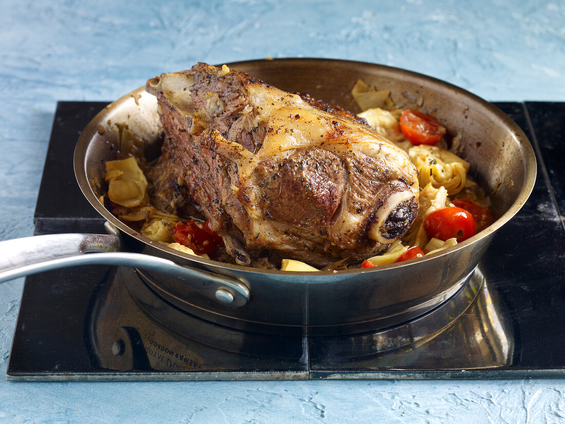 Shoulder of lamb with artichokes and cherry tomatoes in pan