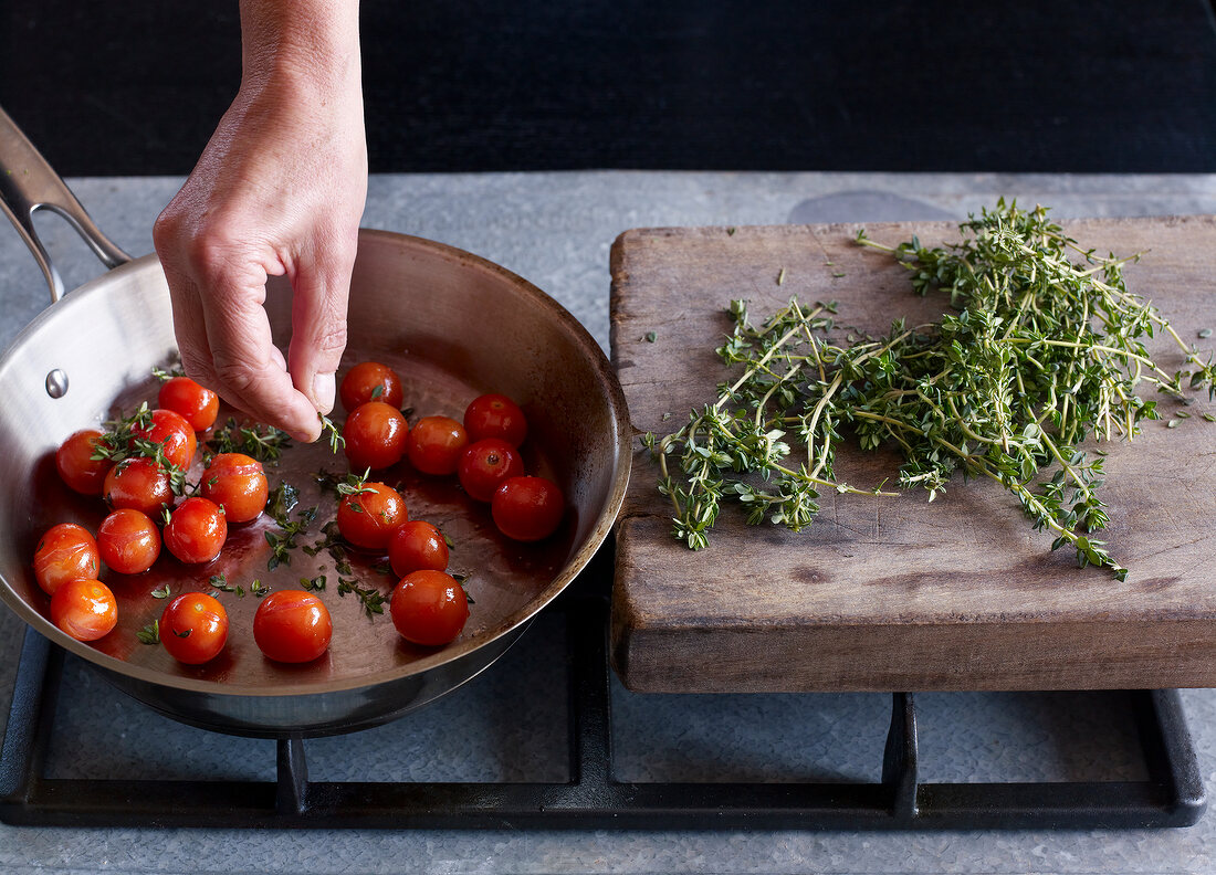 Close-up of hand adding herbs on roasted cherry tomatoes in pan