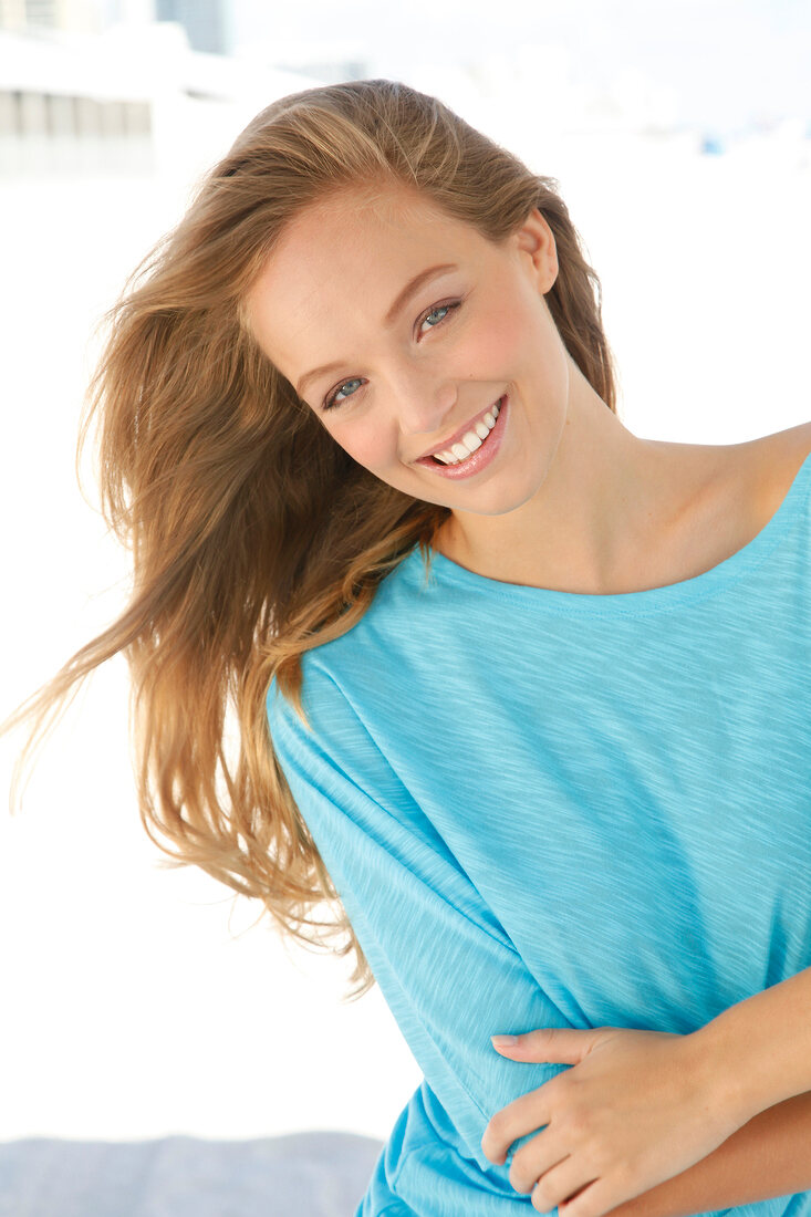 Portrait of beautiful blonde woman wearing turquoise to with arms crossed, smiling