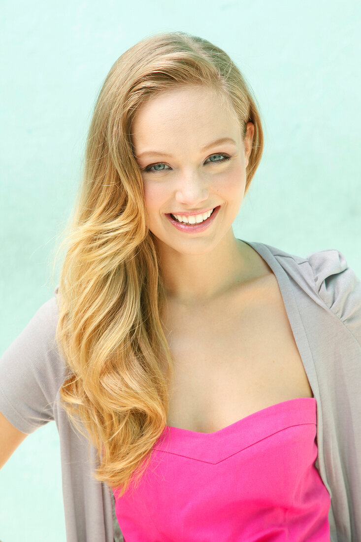 Portrait of beautiful blonde woman wearing gray cardigan over pink top, smiling