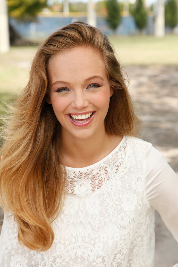 Portrait of happy blonde woman with long hair wearing white lace top, laughing