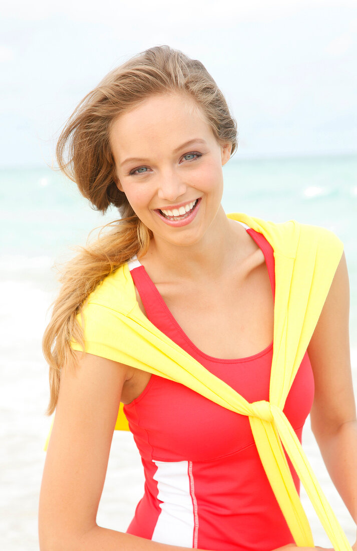 Portrait of pretty woman wearing red sporty top and yellow coat over shoulder, smiling