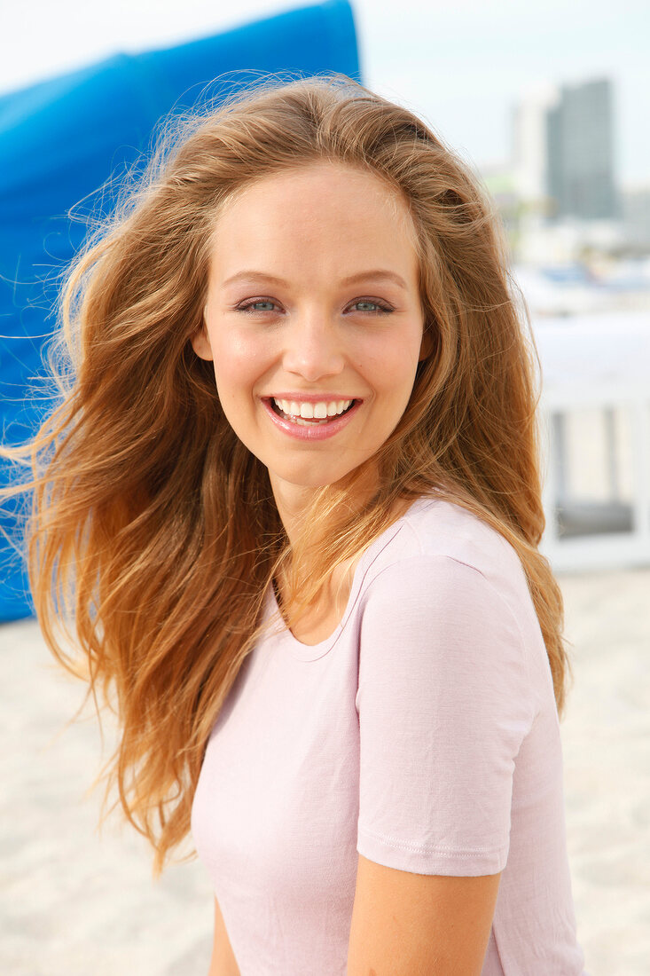 Portrait of beautiful blonde woman with windswept hair wearing pink top, smiling
