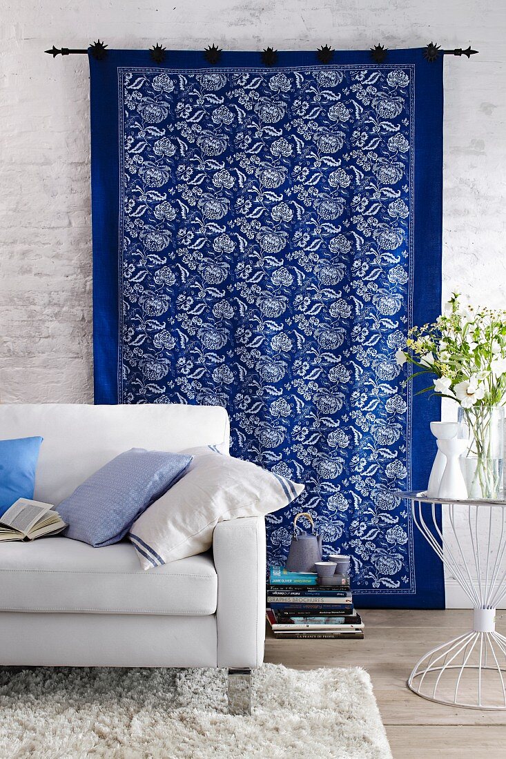 Blau-weiss bedruckter Wandbehang hinter weißem Sofa im Wohnzimmer