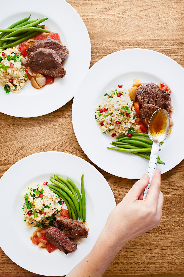 Beef fillet with pomegranate couscous and green beans on plates, overhead view