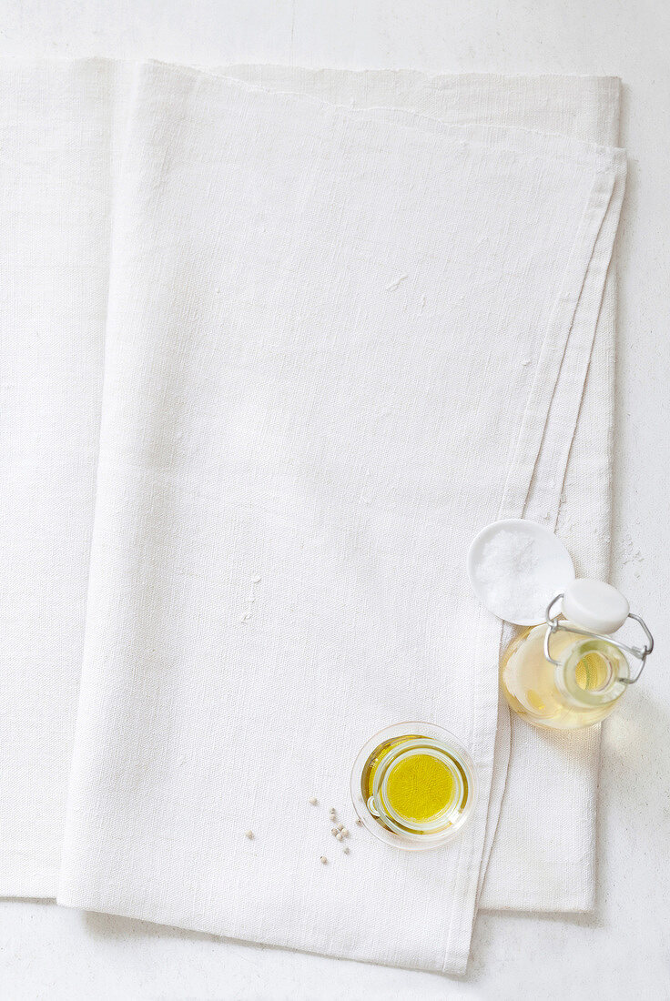 Glass jar and bottle of oil with salt in bowl on white towel