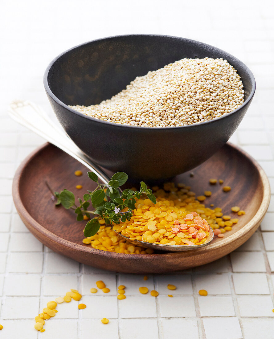 Yellow lentils on wooden plate with spoon and quinoa in wooden bowl