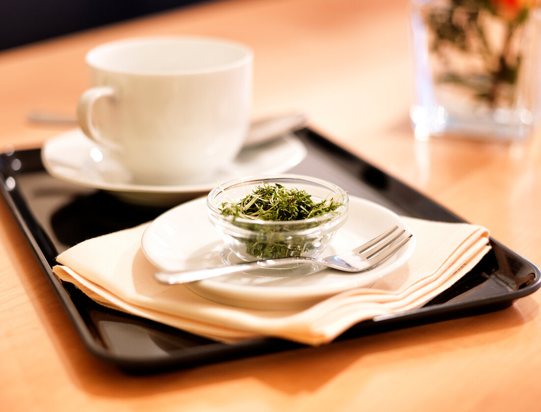 Sprossen in einem Glasschälchen, Tablett mit Teetasse