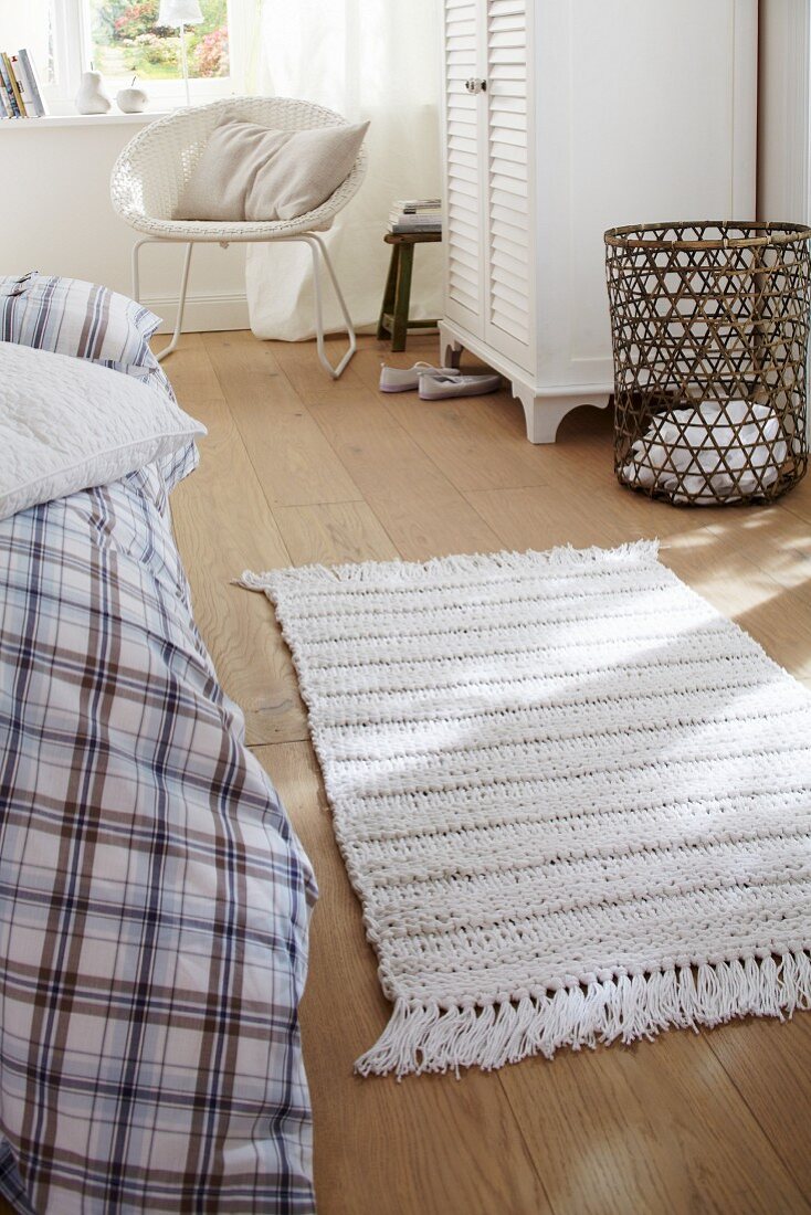 Weißer gestrickter Teppich auf Holzdielen im Schlafzimmer