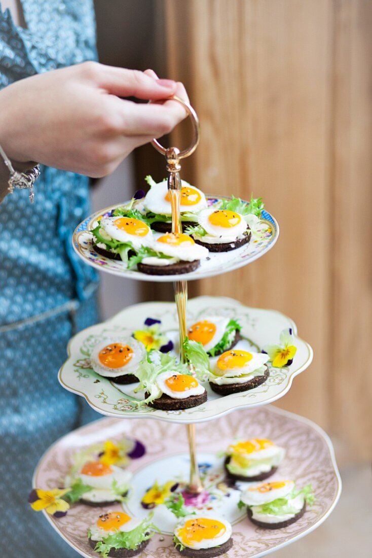 Fried eggs on pieces of pumpernickel on a cake stand