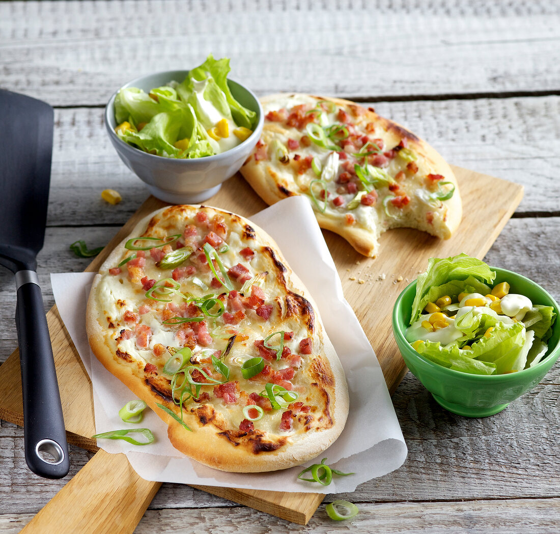 Quiche on wooden board with salad in bowl
