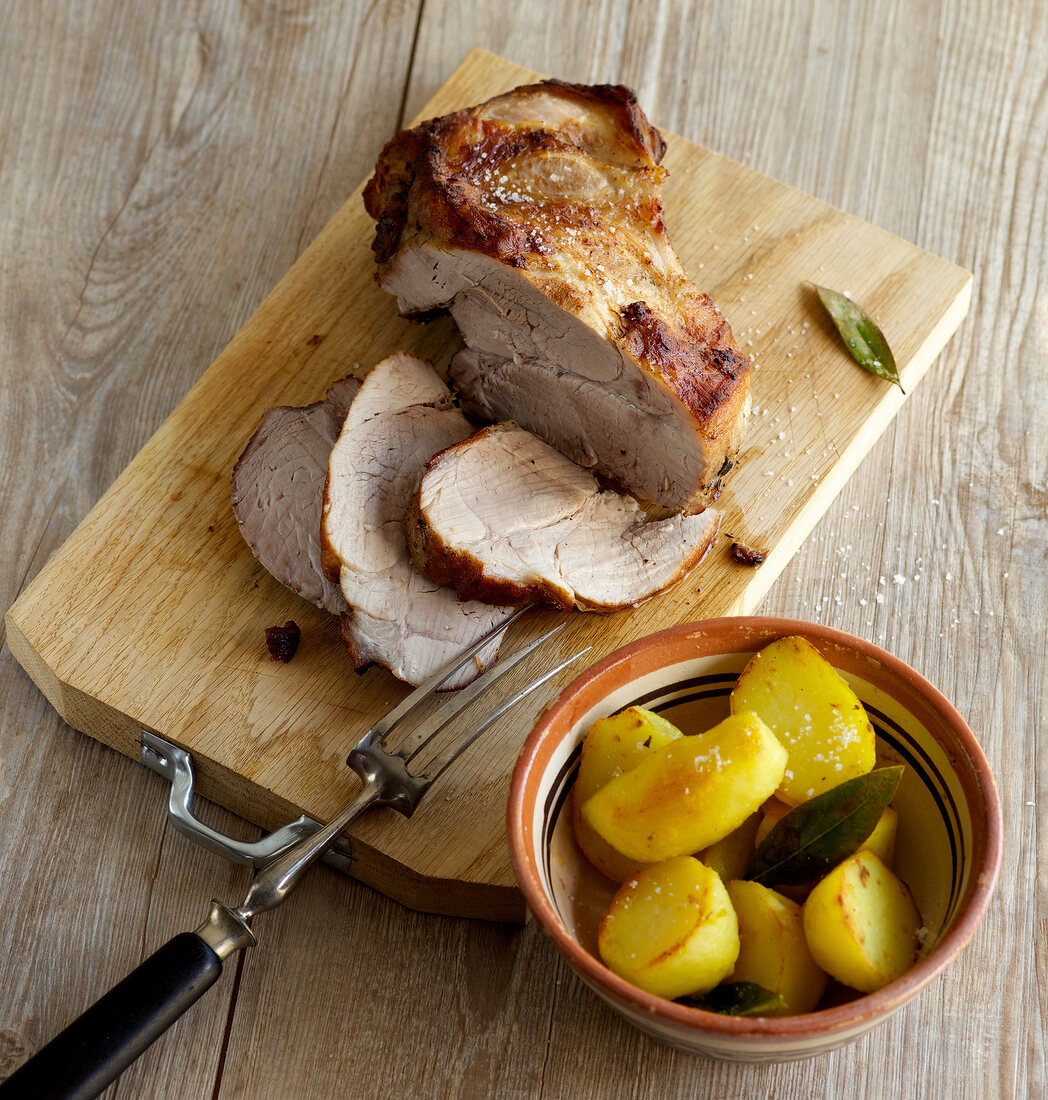 Roast pork on wooden board with bay potatoes in bowl