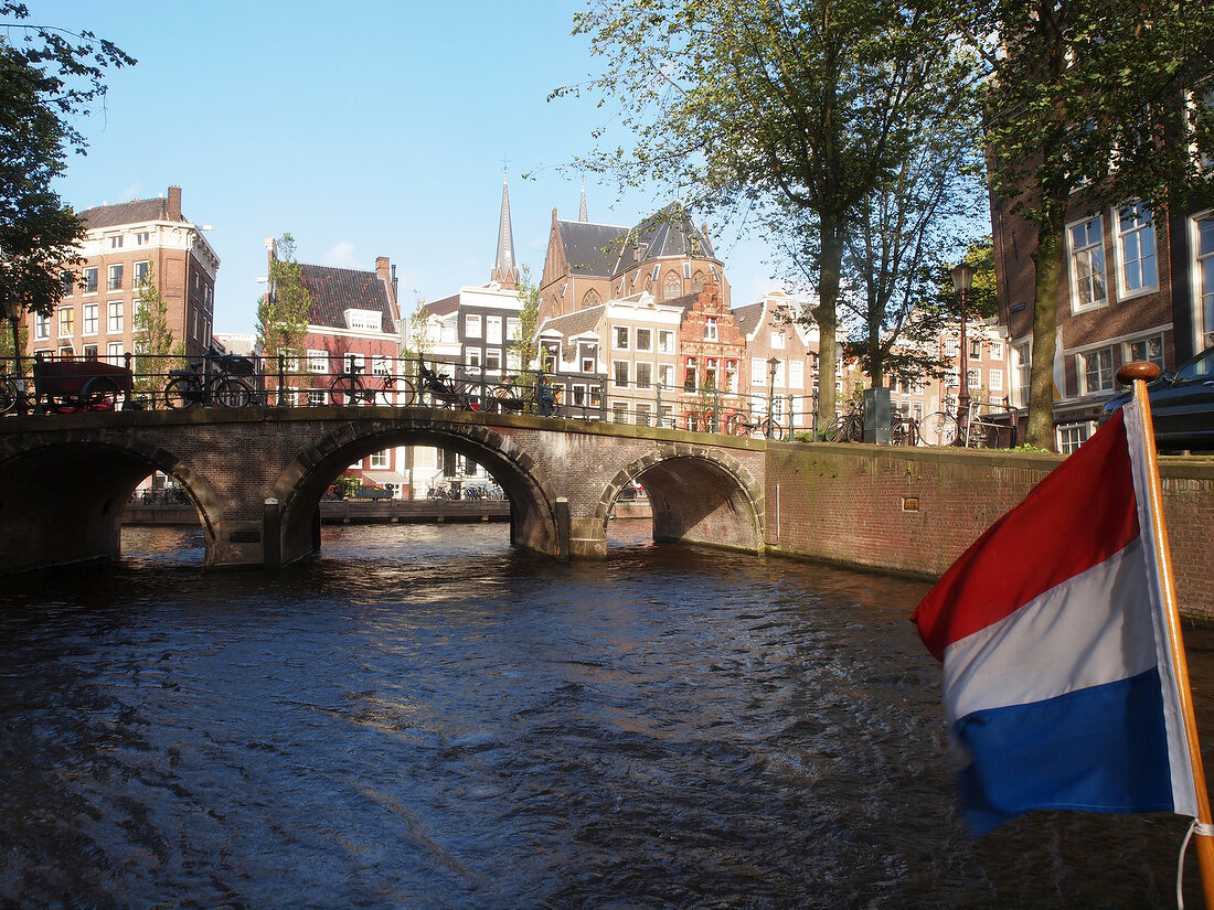 View of historic canal houses from boat with flag at Canal of Amsterdam, Netherlands