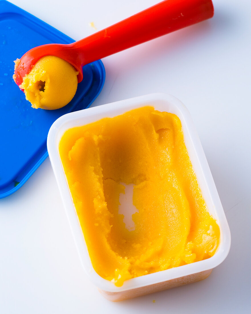 Mango sorbet in container and ice-cream scoop