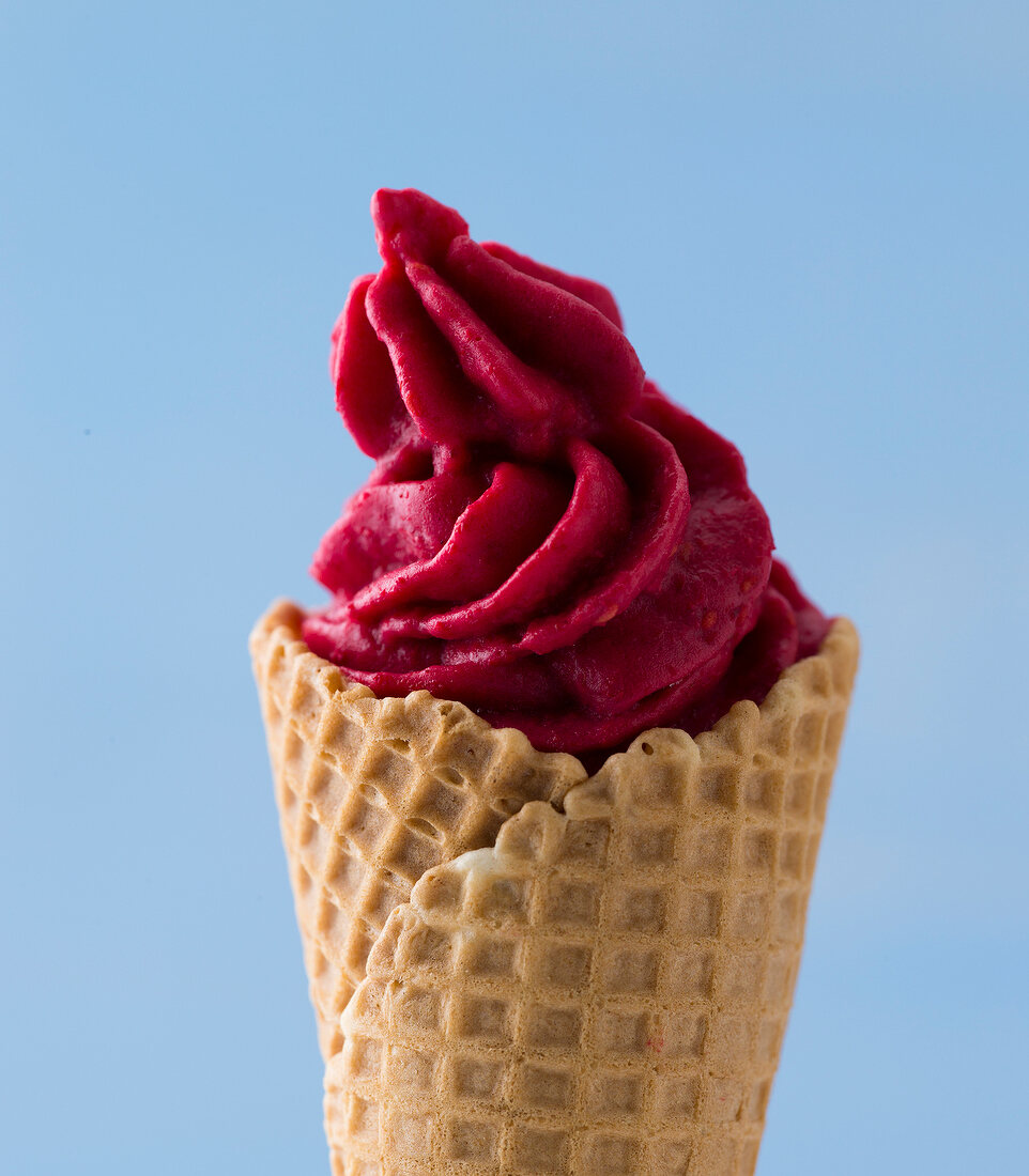 Close-up of raspberry ice-cream in waffle cone against blue background