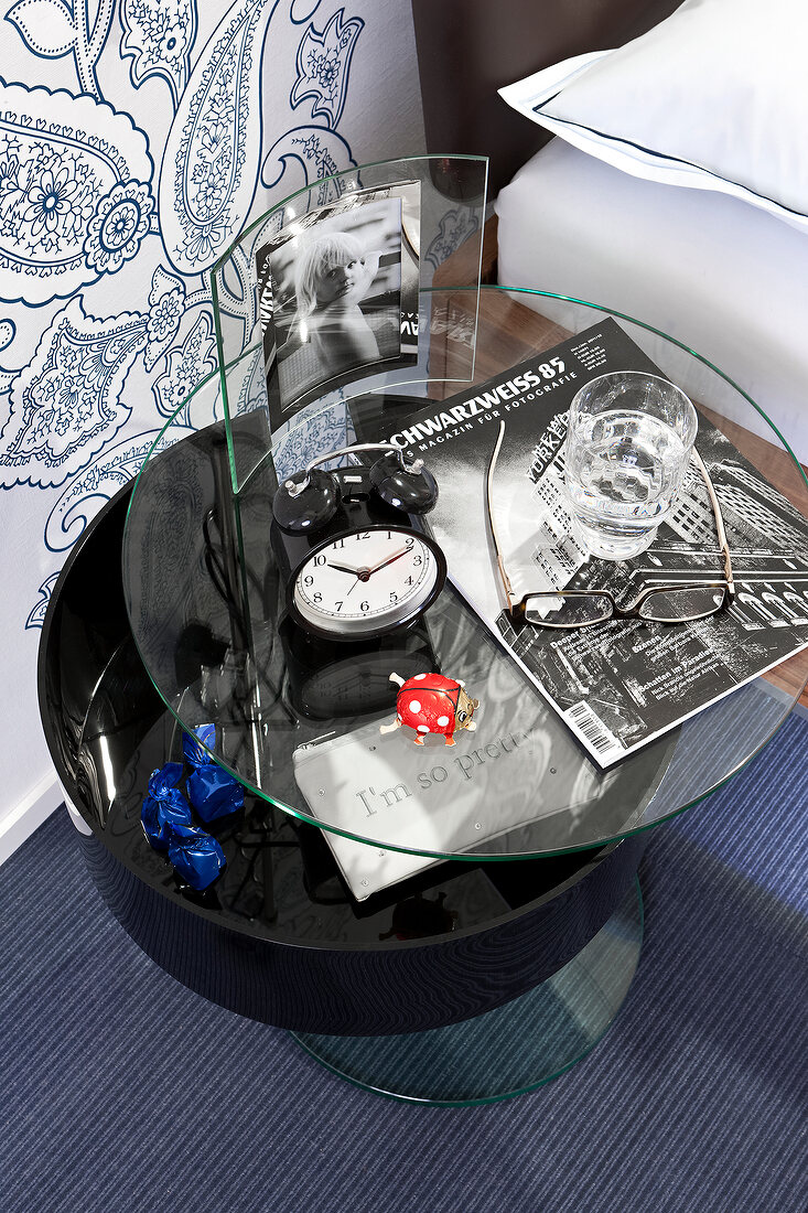 Glass table with alarm clock, glass and magazines