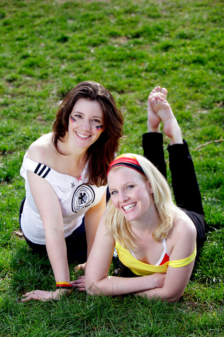 Portrait of two beautiful woman lying on grass, smiling