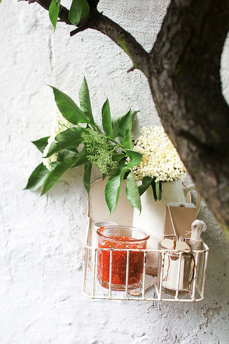 A basket of rhubarb and elderberry jam and elderflowers on a wall