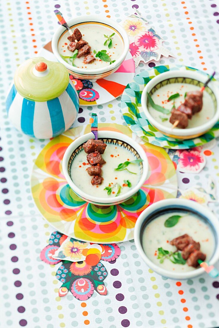 Sellerie-Kräuter-Rahmsuppe mit Lammspießen auf bunt dekoriertem Tisch