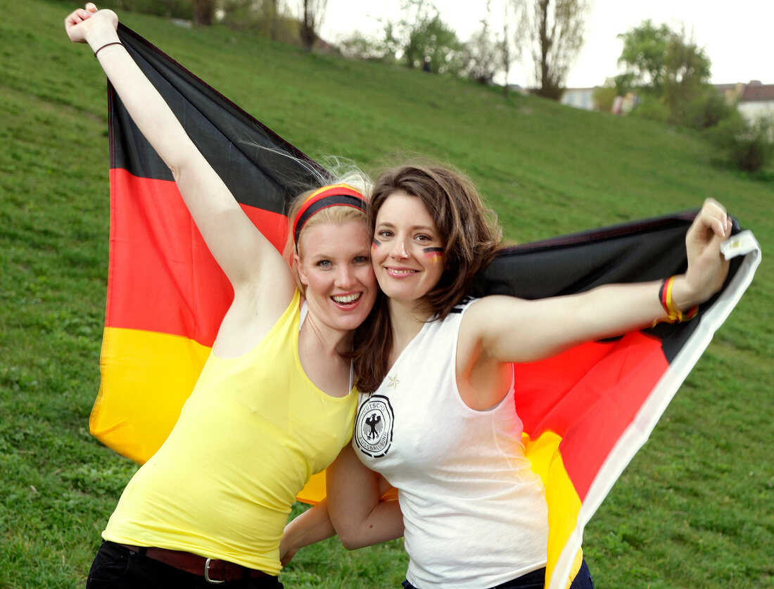 Portrait of two beautiful woman holding Germany flag behind them