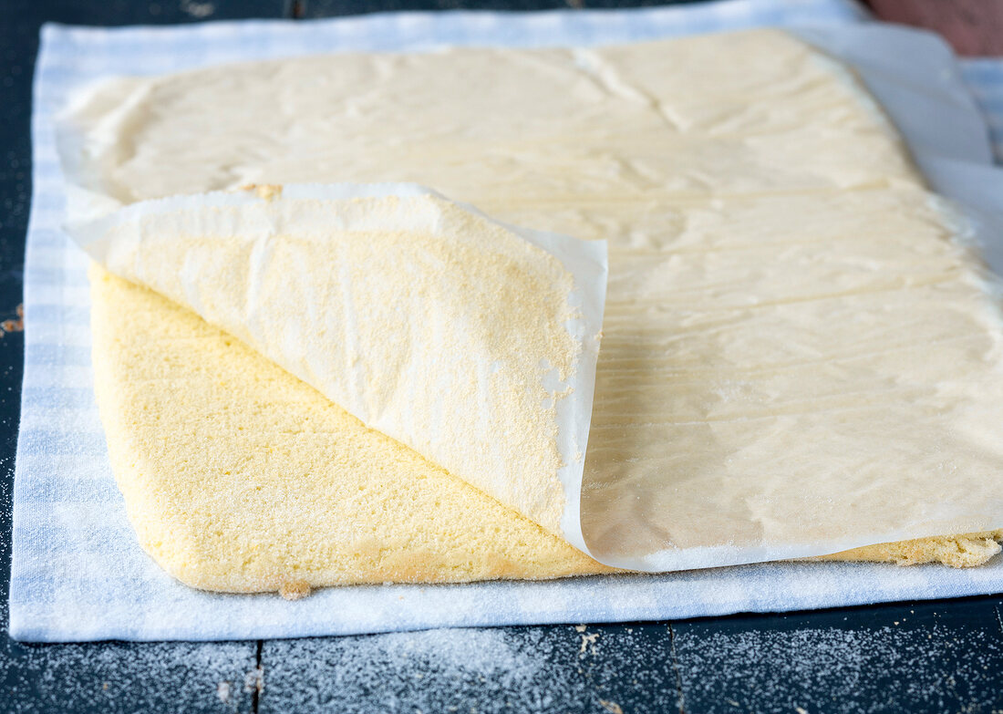 Baking paper being removed from sponge base for preparation of cheese cake, step 2