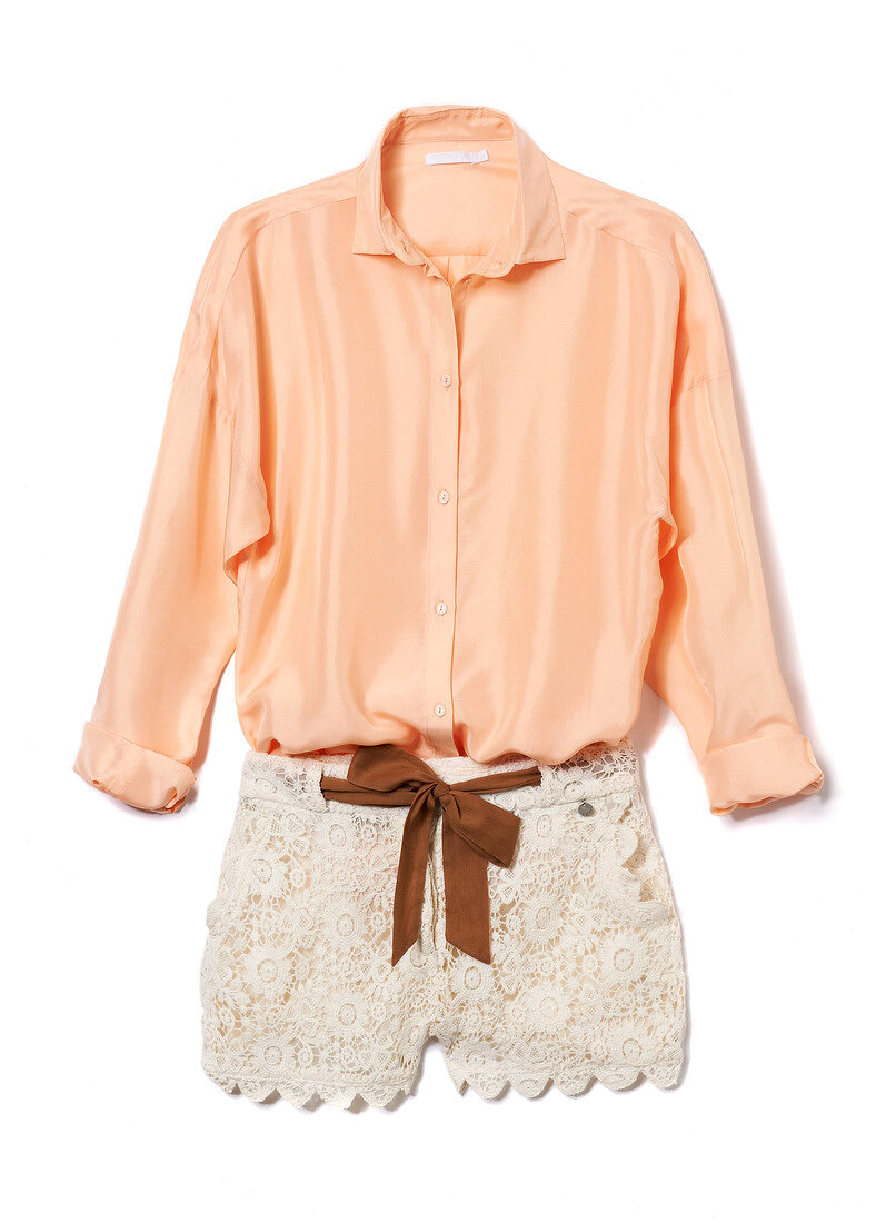 Close-up of peach silk blouse and lace shorts on white background