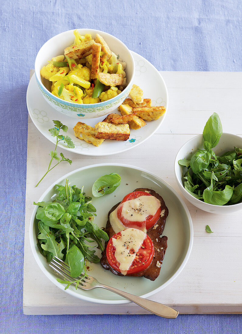 Tempeh with curried vegetables and seitan salad on plates