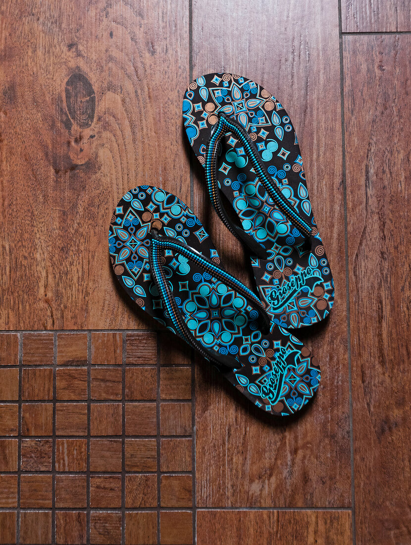 Pair of blue and black thong patterned flip flop on wooden floor