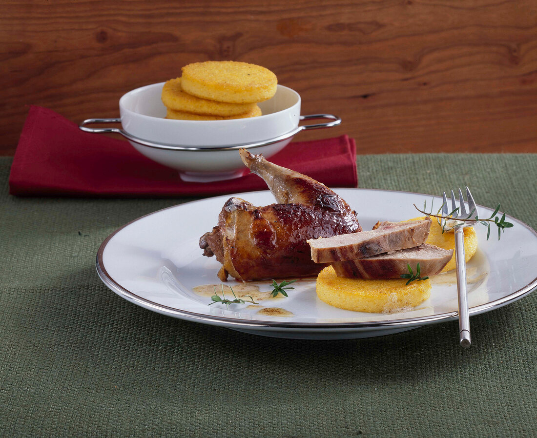 Wild pheasant poached in herb cream with orange polenta on plate