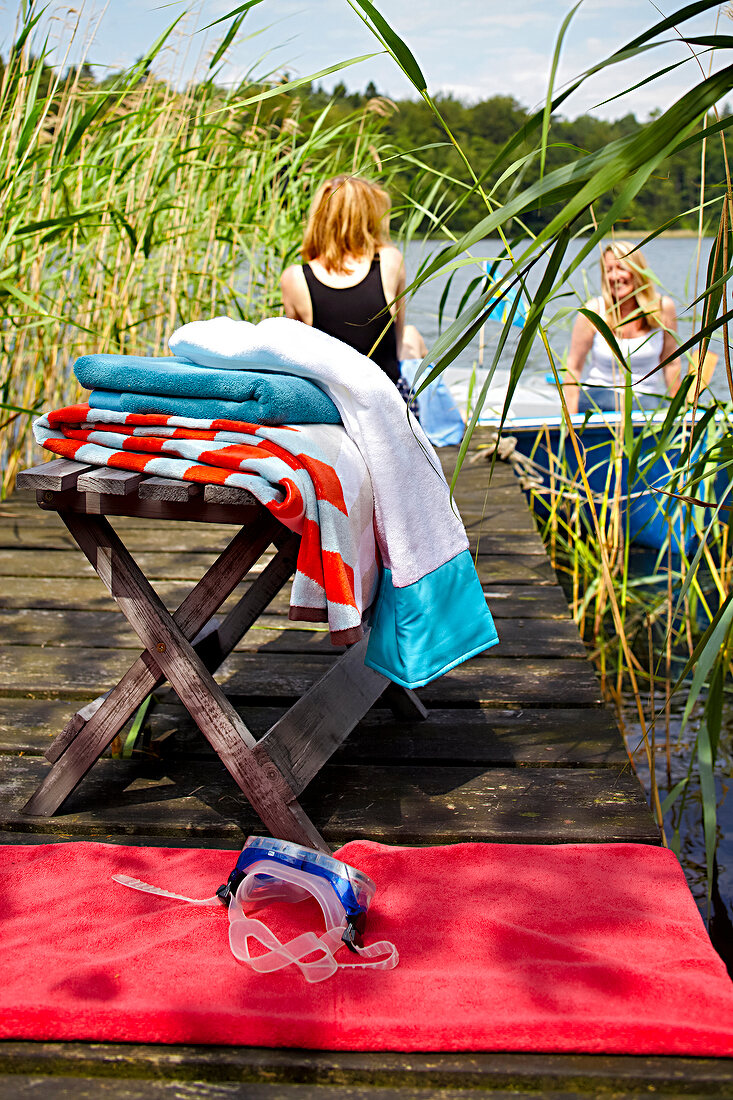 Women at lakeside with reed grass with scuba mask on red towel and on stool