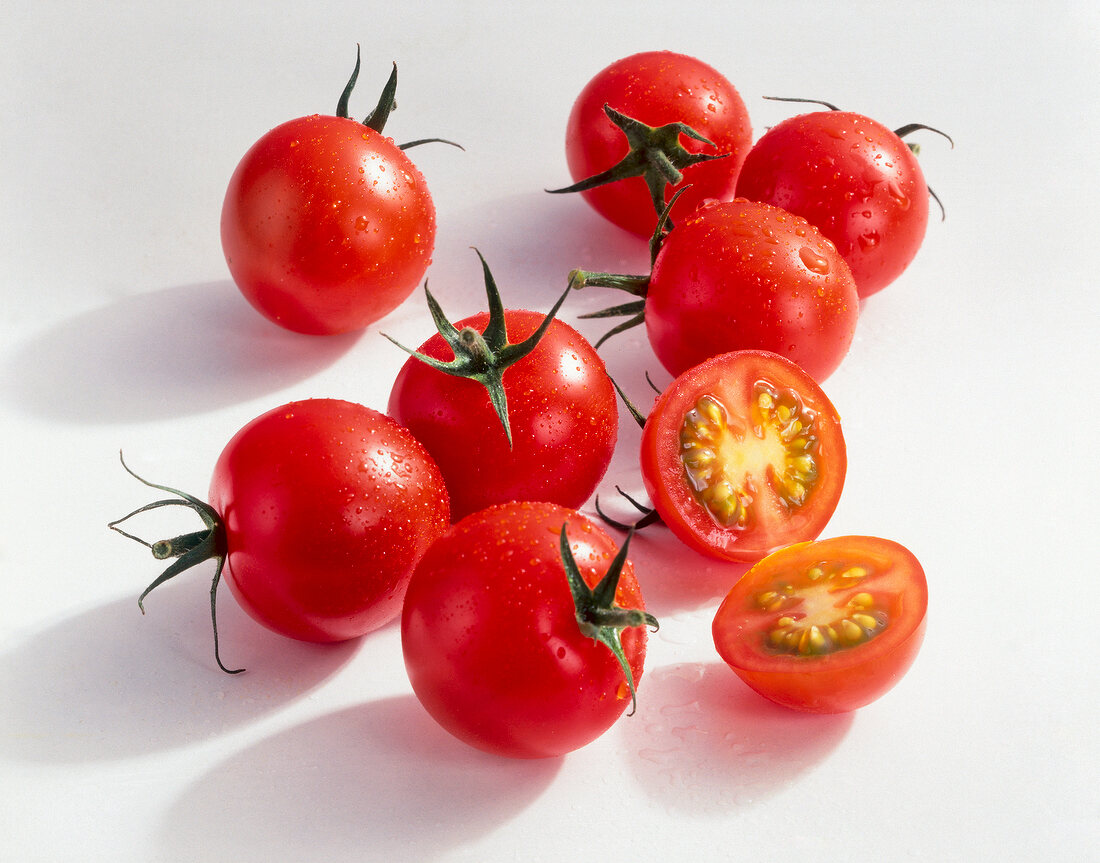 Halved and whole cherry tomatoes on white background