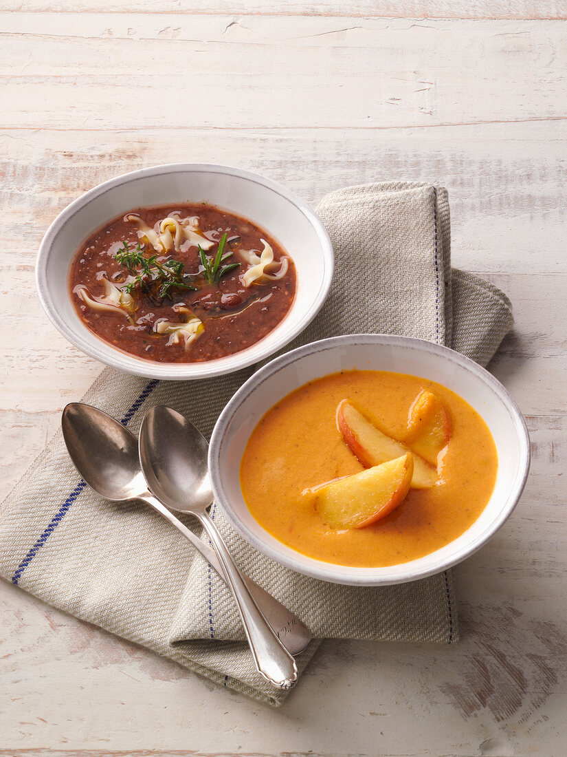 Two bowls of bean soup with noodles and carrot-ginger soup