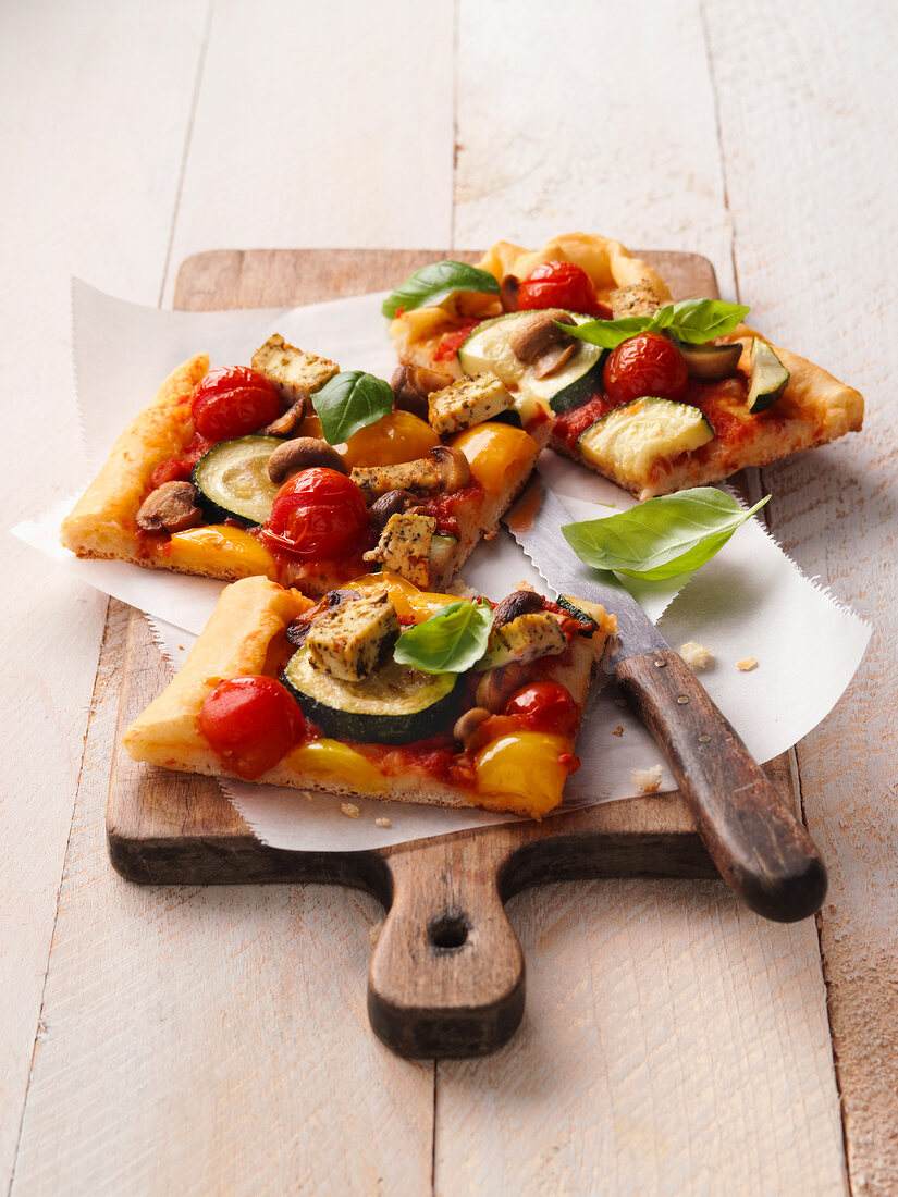 Vegetable pizza slices with knife on wooden serving board